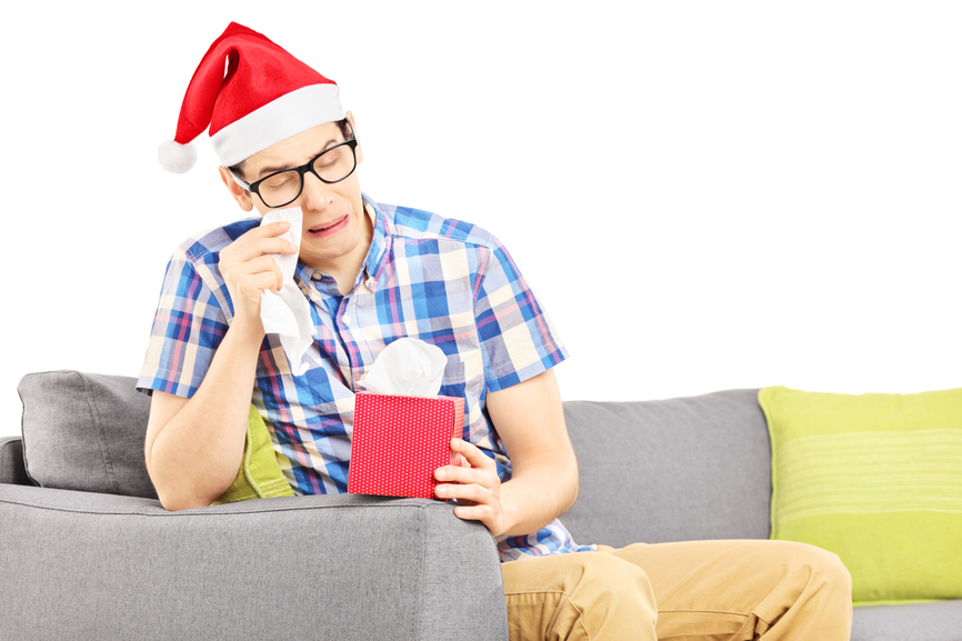 Sad guy with santa hat on a sofa wiping his eyes from crying